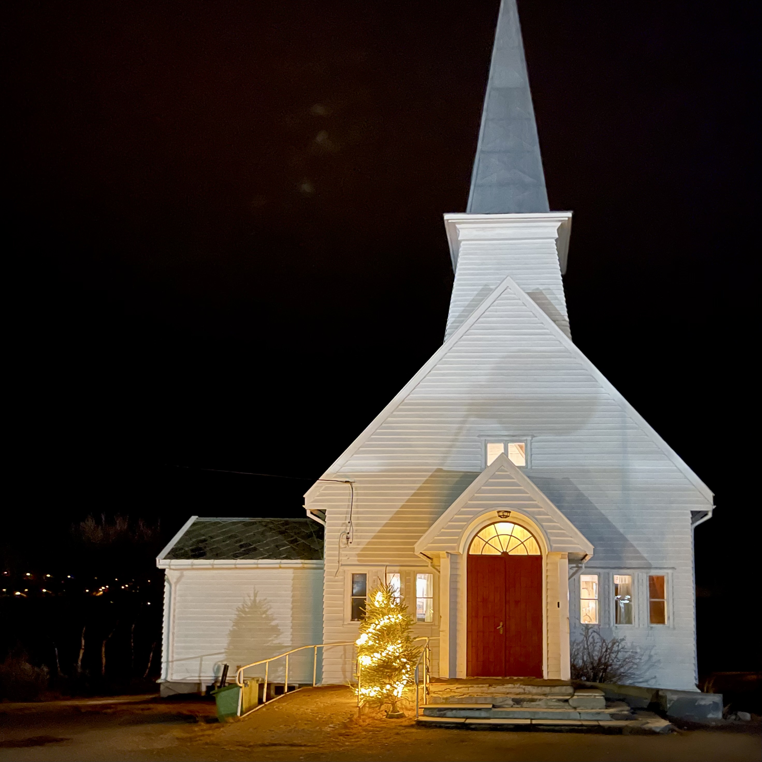 Valkoinen kirkkorakennus, jossa valaistus pimeän aikaan.