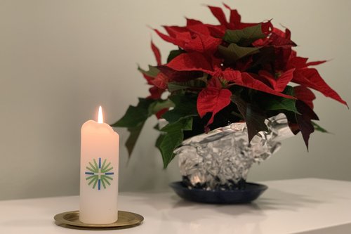 Palava kynttilä, jossa on seurakunnan logo ja punainen joulutähti toimiston pöydällä.